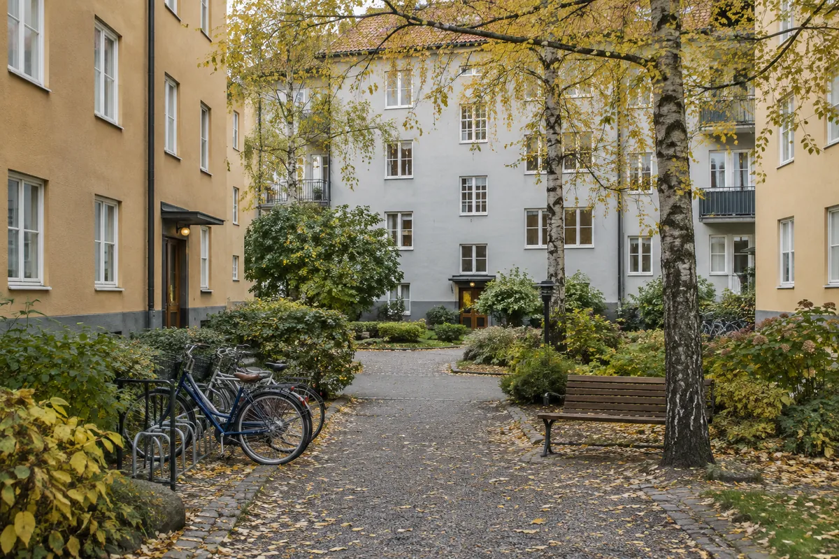 Innergård i en bostadsrättsförening med cyklar, björkar i höstfärger och en parkbänk